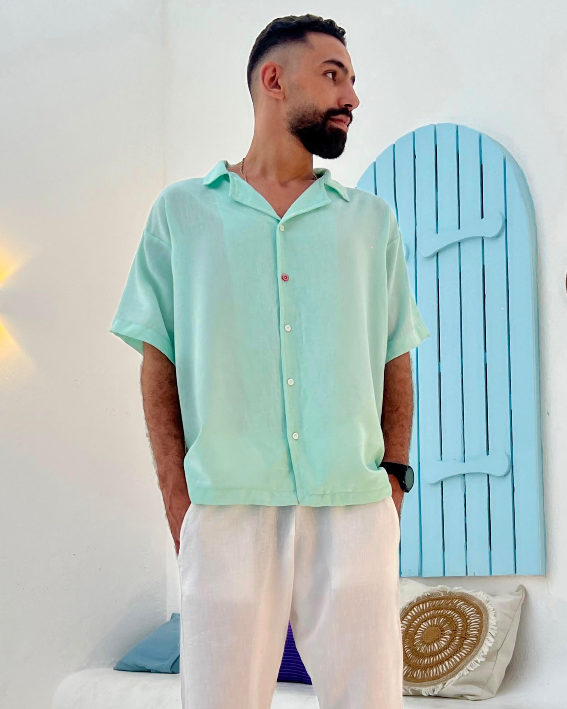 Man wearing a light green shirt standing in a room with a blue door and yellow light fixture.